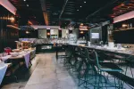 Innenansicht eines modernen Restaurants mit langen Tischen und Barbestuhlung