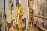 Person in gelber Jacke neben Kamin mit Werkzeugen