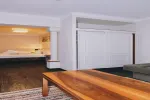 Innenraum mit Holztisch, weißen Wänden und einem Blick auf ein Schlafzimmer.