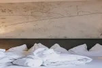 Bett mit zerknitterten weißen Laken und einer strukturierten Wand dahinter
