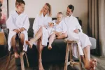 Familie in Bademänteln sitzt auf Hockern neben einem Sofa