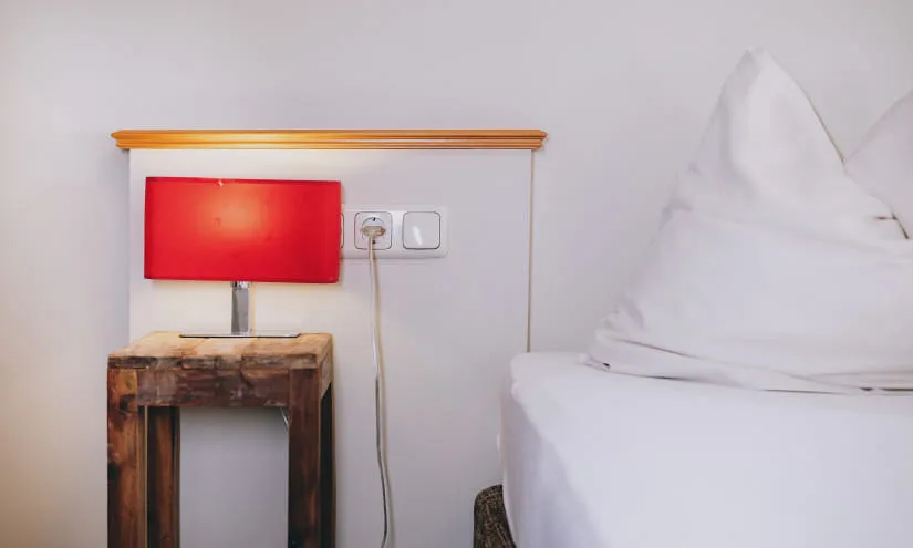 Ein Nachttisch mit roter Lampe und Steckdose neben einem Bett