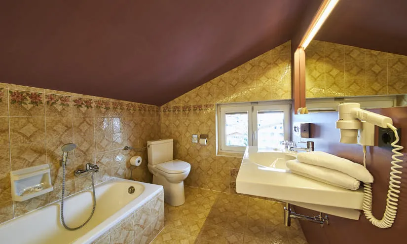 Badezimmer mit Badewanne, Toilette und Waschbecken unter schrägem Dach