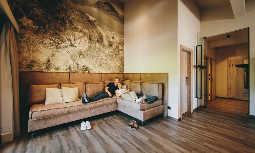 Helles Wohnzimmer mit einer Couch und Holzfußboden, im Hintergrund eine Landschaft.