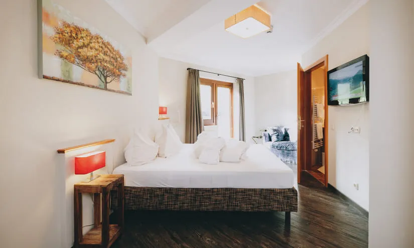 Helles Zimmer mit Doppelbett, Tischlampe und Fenster.