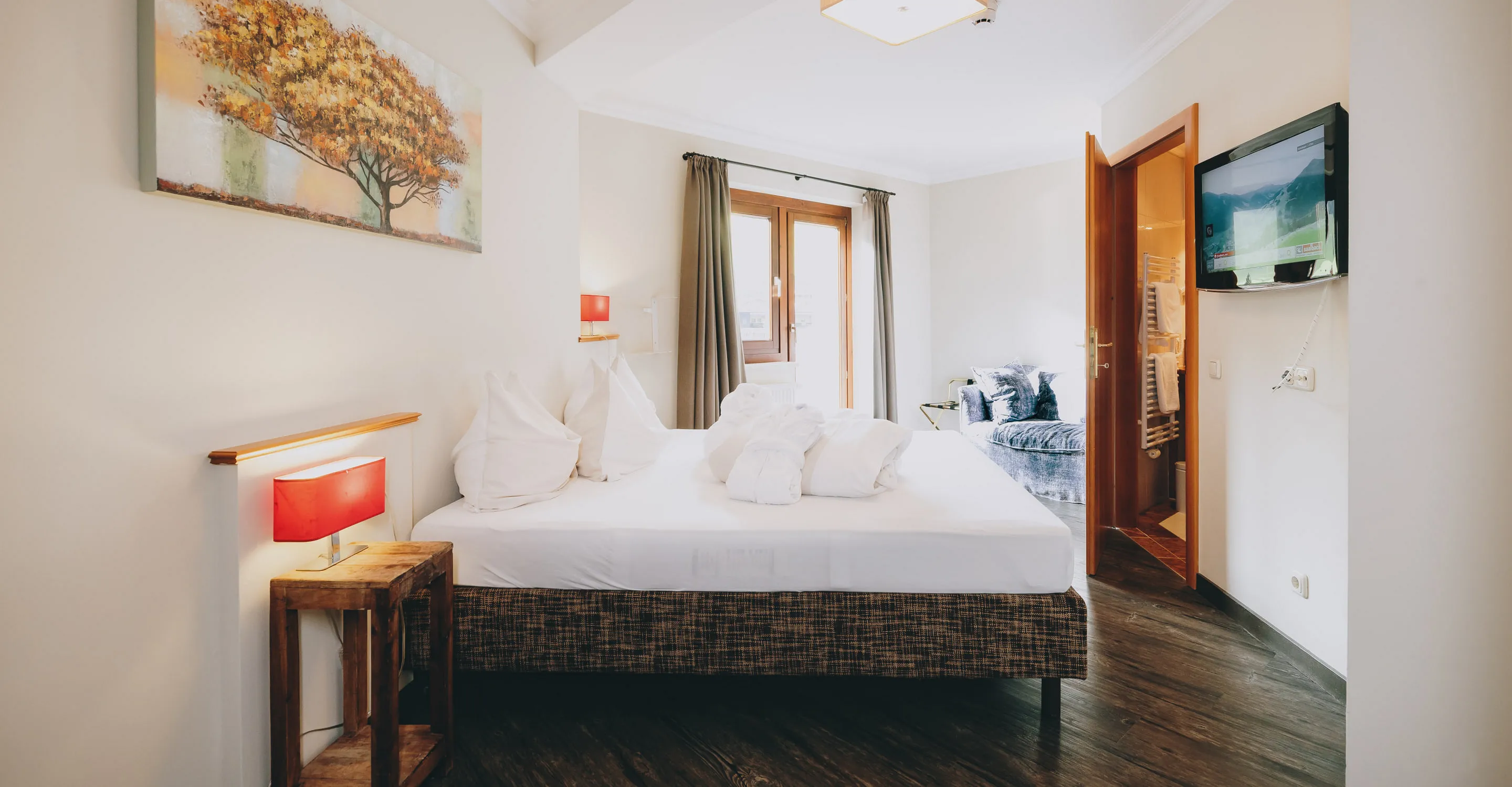 Helles Zimmer mit einem Doppelbett, Sitzbereichen und Fernseher.