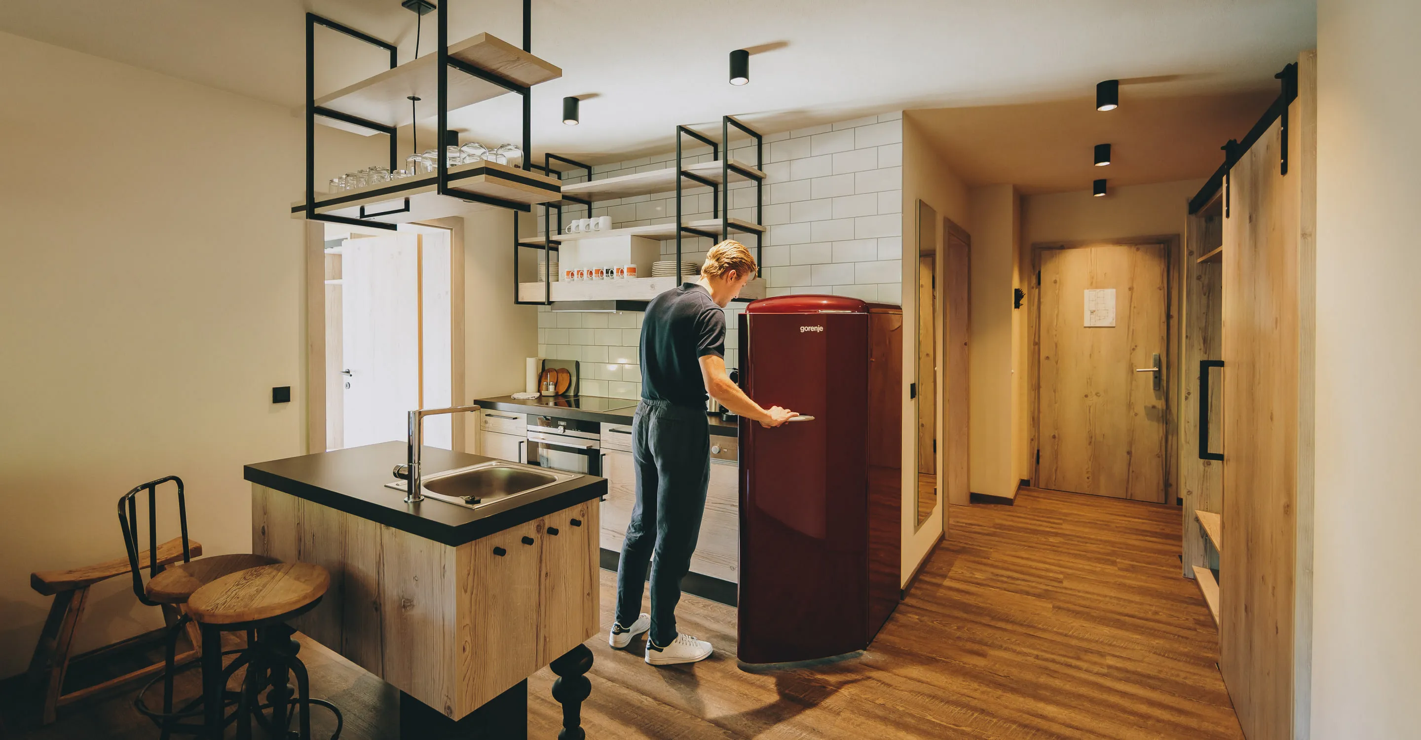 Moderne Küche mit Holzregalen und rotem Kühlschrank, Person am Kühlschrank