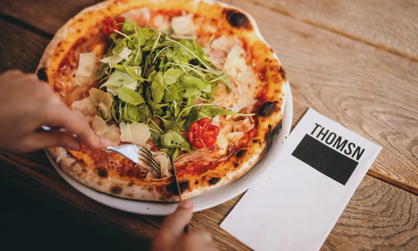 Pizza mit Salatbeilage auf einem Teller, daneben eine Menükarte von THOMSN