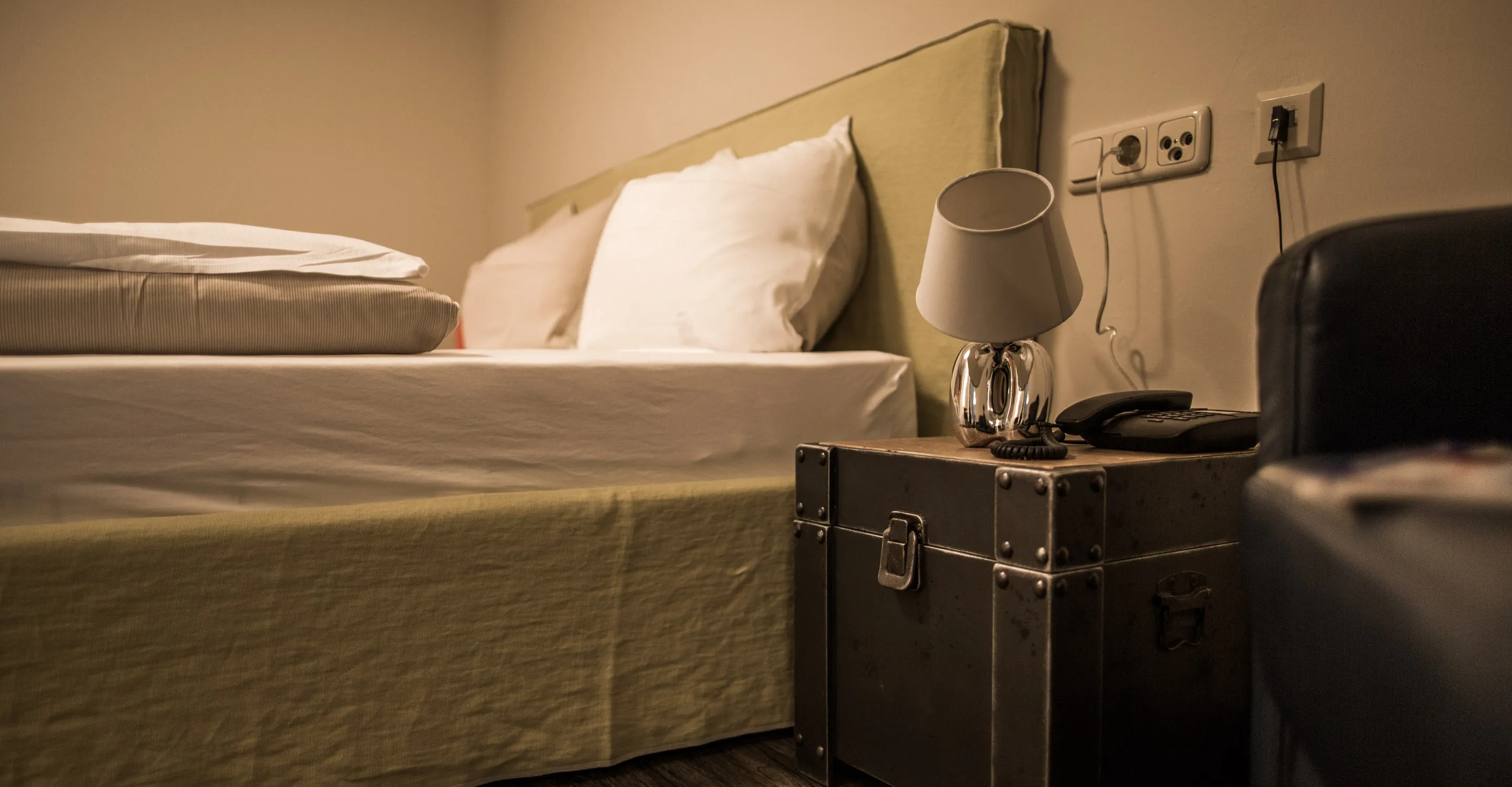 Innenansicht eines Zimmers mit Bett, Nachttisch und Lampe