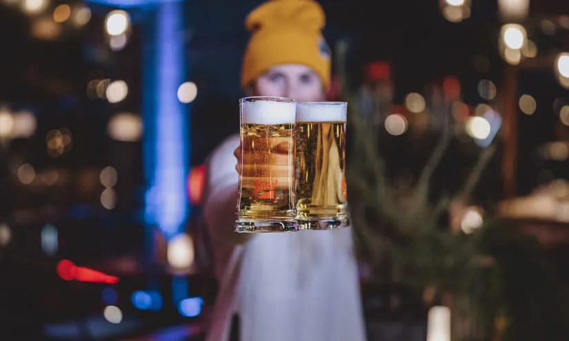 Person hält zwei Biergläser in einer Bar-Umgebung