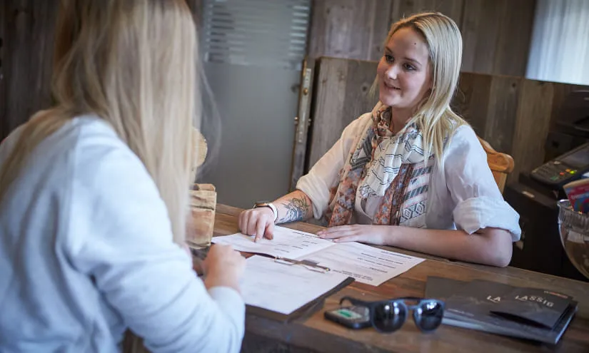 Zwei Frauen am Empfangstresen, die Unterlagen in einer gemütlichen Umgebung besprechen.