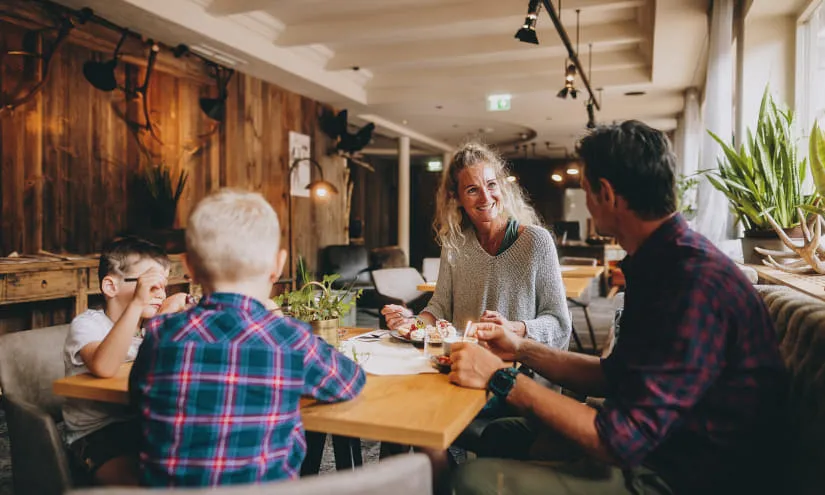 Familie in einem Restaurant, Frau spricht mit Mann und Kinder am Tisch.