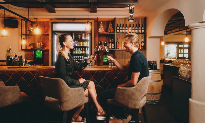 Zwei Personen in einer Bar, sie stoßen mit Drinks an.