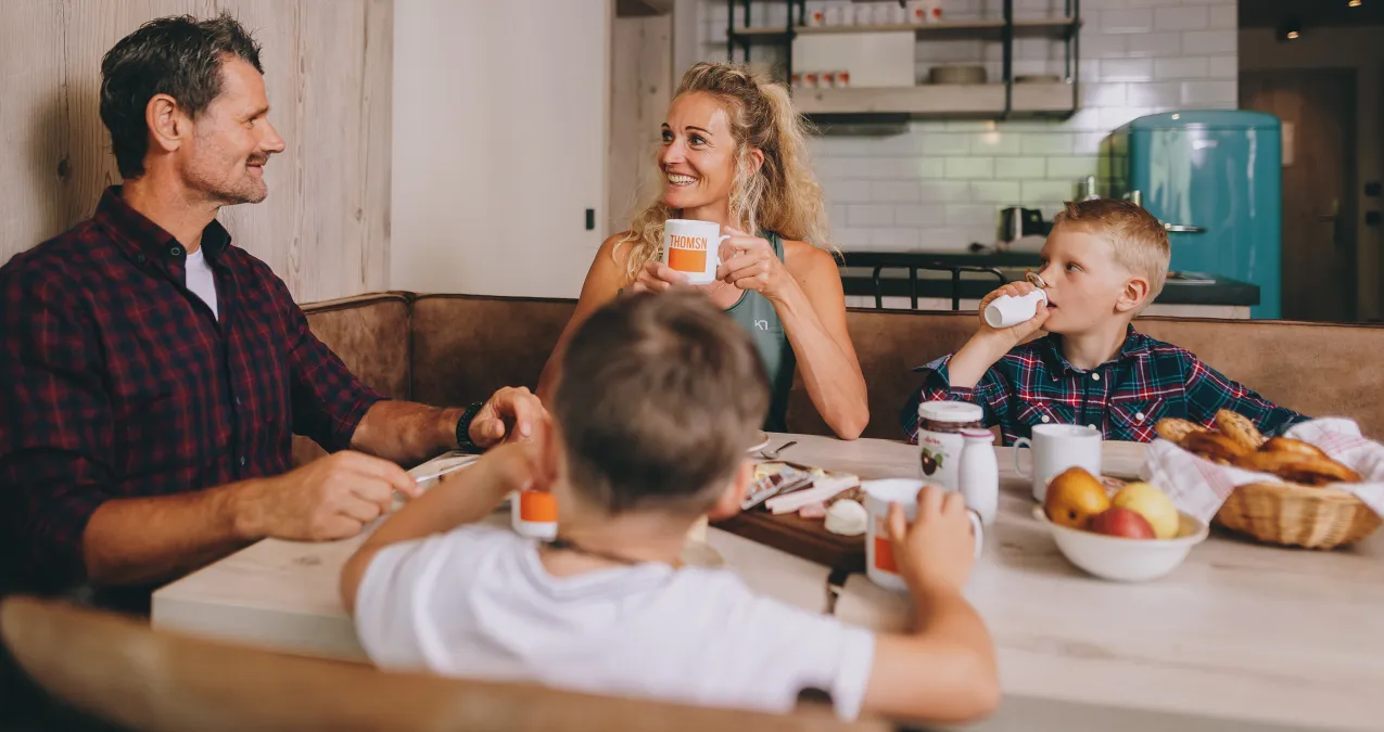 Family sitting at a table with food and drinks in a modern kitchen.