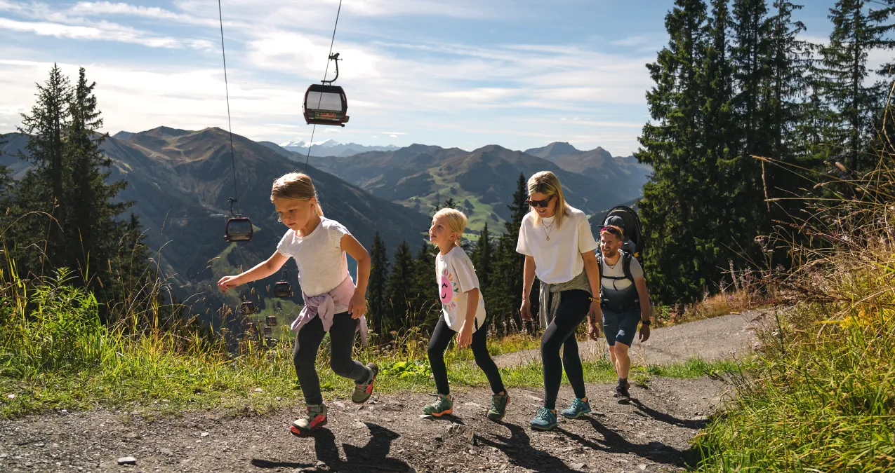 Familie wandert auf einem Bergweg mit Seilbahn im Hintergrund