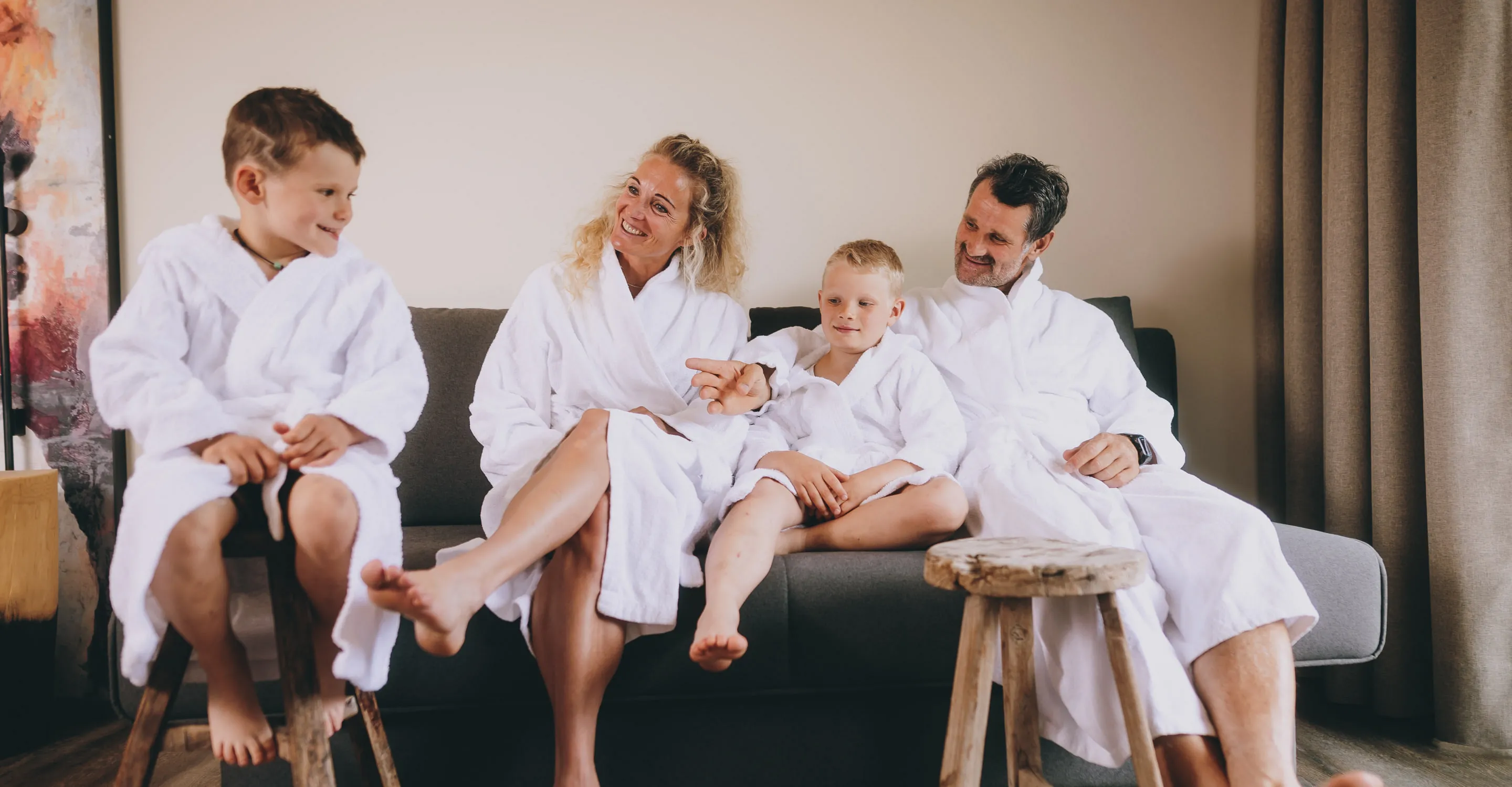 Familie in weißen Bademänteln sitzt lachend auf einer Couch.