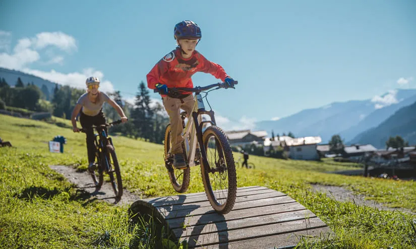Zwei Kinder radfahren in einem Park mit Bergen im Hintergrund