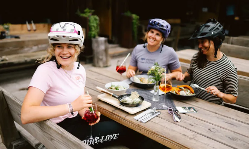 Drei Frauen mit Schutzhelmen, die am Tisch essen und trinken.